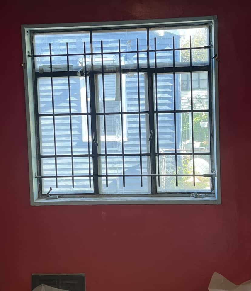 Old single-pane window behind metal security bars in a bedroom with red walls